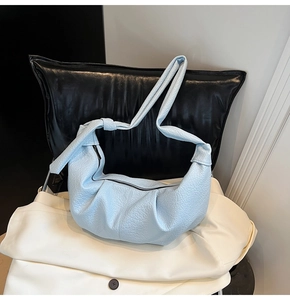 Detail of light blue crescent bag with pleated leather texture and knotted wide shoulder strap