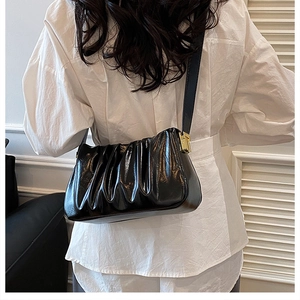 Detail of a black pleated cloud bag on model's shoulder with golden buckle accent