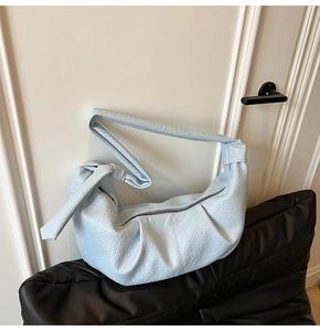 Close-up of light blue pleated croissant bag with knotted strap and metal zipper
