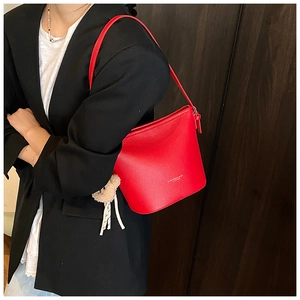 Detail of red lychee textured leather bucket bag with gold logo and plush bear charm