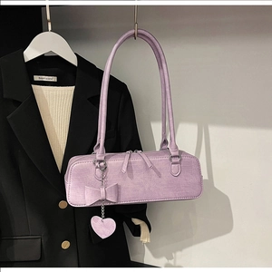 Détail du sac violet gaufré croco avec nœud et breloque cœur sur un costume