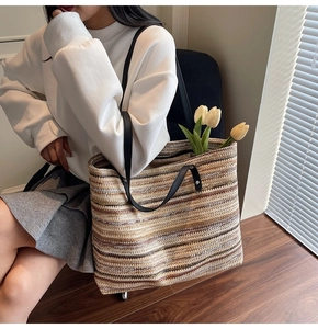 Large striped straw tote bag with black leather handles shown on model in a modern room