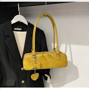 Détail du sac baguette jaune à motif crocodile avec nœud et pendentif en cœur