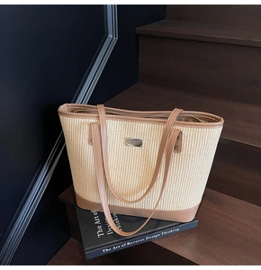 Close-up of woven straw tote bag with brown faux leather trim and metallic plate