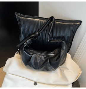 Detail of black pebbled leather croissant bag with pleated design and knotted shoulder strap