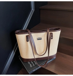 Detail of woven straw tote bag featuring dark brown leather trim and metal nameplate