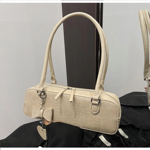 Détail du sac à bandoulière crème motif crocodile avec nœud en cuir et pendentif cœur