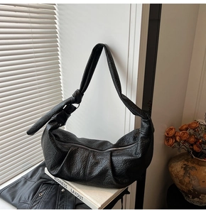 Detail of black pleated shoulder bag with knotted strap and zipper closure on a windowsill