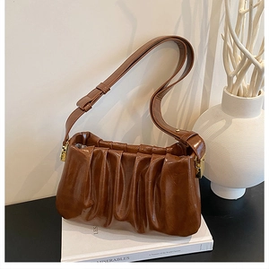 Close-up of brown pleated cloud bag featuring glossy finish and gold metal buckle