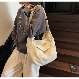 Close-up of beige canvas shoulder bag with front flap pocket and raw edge detail