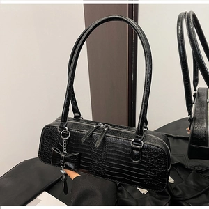 Détail d'un sac à main noir motif crocodile avec zips argentés et pendentif nœud