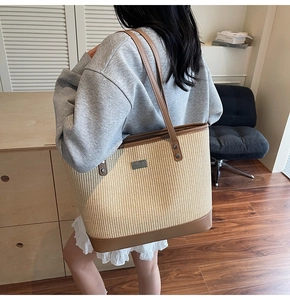Detail of large straw tote bag featuring brown leather trim and metal logo plaque