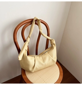Detail of cream pleated leather crossbody bag with knot shoulder strap on wooden chair
