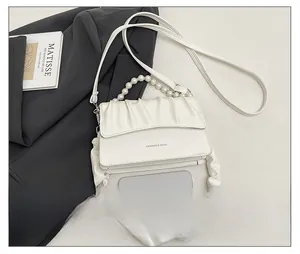 Close-up of white ruched cloud bag with pearl handle and shoulder strap next to phone