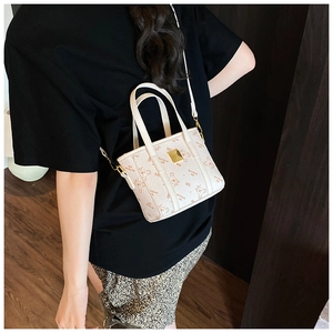 Detail of printed beige mini tote bag worn crossbody with adjustable shoulder strap