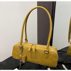 Détail du sac sous le bras jaune à texture crocodile et pendentif nœud décoratif