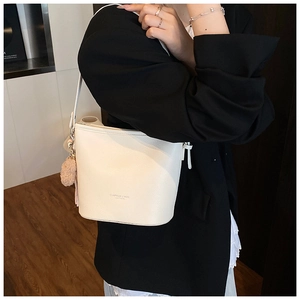 Close-up of white lychee-patterned bucket bag with beige fur ball charm and long strap