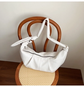 Detail of white pleated croissant bag with knotted shoulder strap on a wooden chair