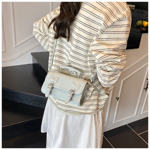 Light blue crossbody bag with bow embossing and dual buckle straps on a casual outfit