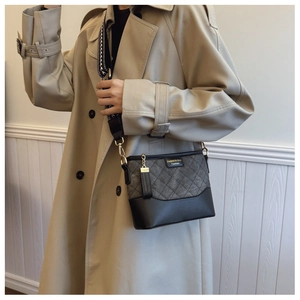 Detail of grey quilted crossbody bucket bag with wide floral strap on a trench coat