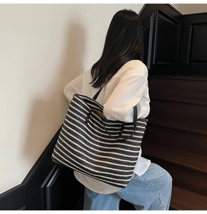Detail of a large striped woven tote bag with premium black shoulder straps on model