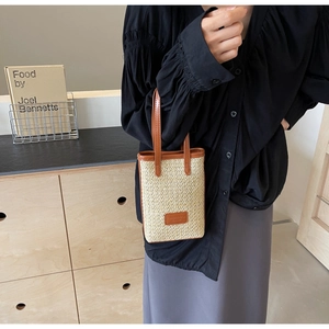 Detail of hand-held beige woven straw bag with premium brown leather trim and brand patch