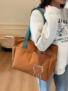 Brown canvas tote bag with teal handles and cat embroidery worn by a model in a room
