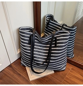 Detail of hand-woven striped tote bag with black leather handles on a dark wood floor