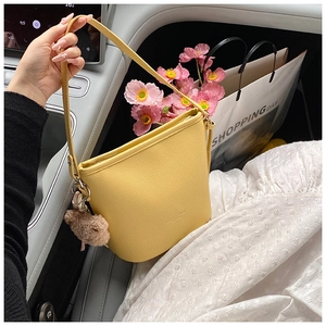 Detail of yellow lychee leather bucket bag with cute plush bear charm in car setting