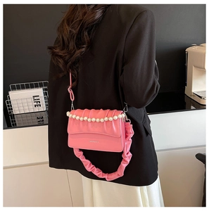 Pink pleated cloud shoulder bag with pearl chain detail worn by model in a modern room
