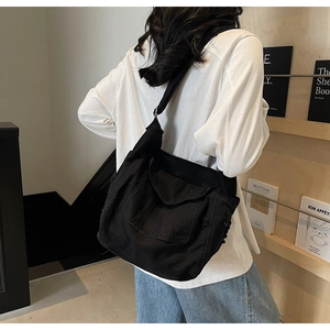 Black canvas tote bag with large front pocket shown on shoulder in a minimalist indoor setting