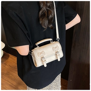Detail view of cream mini bag with metallic bow buckles and adjustable shoulder strap
