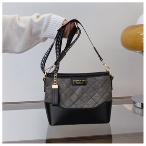 Close-up of quilted grey bucket bag with black leather stitching and wide patterned strap