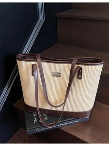 Large woven straw tote bag with brown leather trim and shoulder straps on wooden stairs