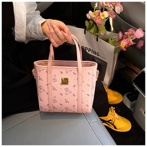 Detail view of pink tote bag with bear print and golden logo plate in a car interior