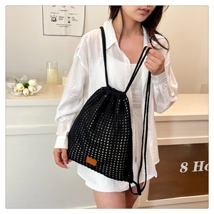 Detail of black crochet drawstring bucket bag with hollow mesh pattern and leather tag