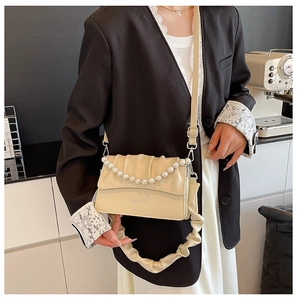 Close-up of cream shoulder bag with pearl handle and pleated strap on a model