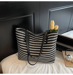 Detail of black and white striped woven tote bag with faux leather straps on white bedding
