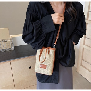 Detail of mini straw crossbody bag with brown leather trim worn over a black shirt