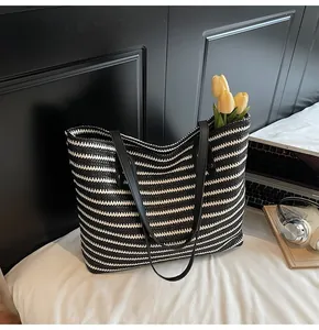 Detailed close-up of woven black and white striped tote bag with elegant black leather handles
