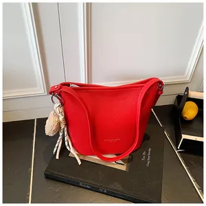 Detail of red pebbled leather bucket bag with a beige plush pompom charm and long strap