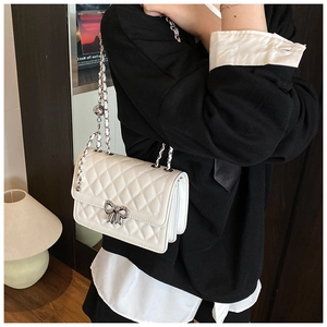 Détail d'un sac à bandoulière matelassé blanc avec boucle nœud argenté et chaîne
