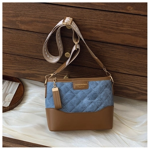 Detail of blue denim quilted bucket bag with brown leather trim and golden hardware