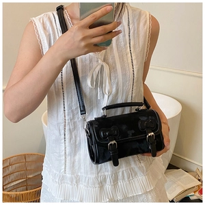 Detail view of a retro black leather crossbody bag with silver buckles and a top handle