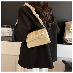 Detail of creamy yellow pleated shoulder bag with elegant pearl chain and matte finish