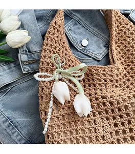Detailed view of tulip charm with green bow and pearl chain on a woven straw tote bag