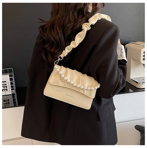 Detail of elegant beige pleated cloud bag with large pearl strap on a woman in black blazer