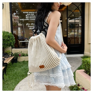 Close-up of cream knitted drawstring backpack with floral hollow pattern for beach vacation