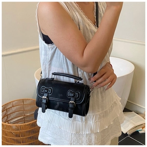 Close-up of black cylinder leather crossbody bag with dual buckle straps and top handle