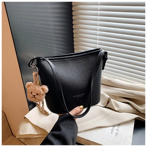 Detail of black bucket bag featuring litchi grain texture and a cute brown bear pendant